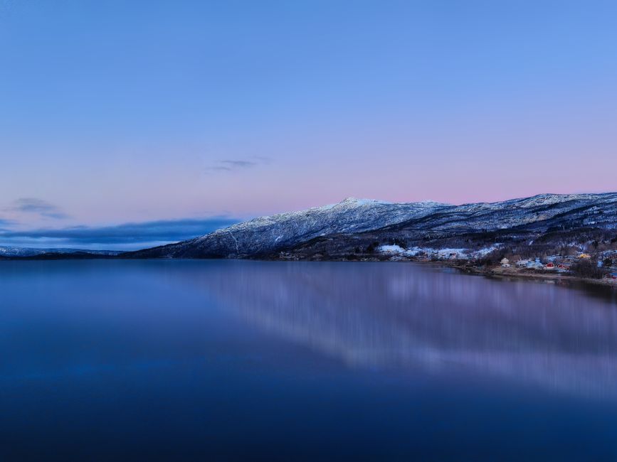 A tranquil, frozen lake in Abisko, Sweden at dawn with snow-capped mountains reflecting the pastel sky.