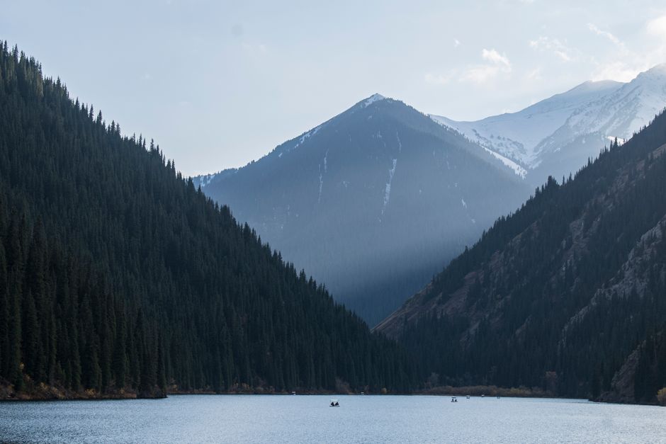 A tranquil mountain lake surrounded by lush pine forests and snowy peaks in Kazakhstan.